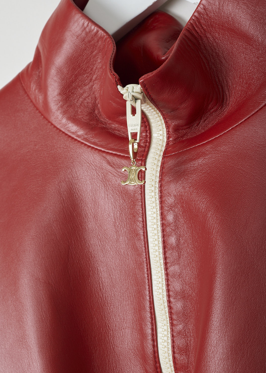 CELINE, TWO-TONE CROPPED LEATHER JACKET, 150T_2EE13_27LV, Red, Beige, Detail, This cropped leather jacket is  two-toned, with the top half in lipstick red and the bottom half and the back in off-white. The jacket has a stand-up collar, two patch pockets with flap and a zipper in a matching off-white color. The gold-tone pull-tab is shaped in the brand's logo. The long sleeves have elasticated cuffs. The elasticated hemline has gold-tone cord locks on the inside. The jackets has a single inner pocket

