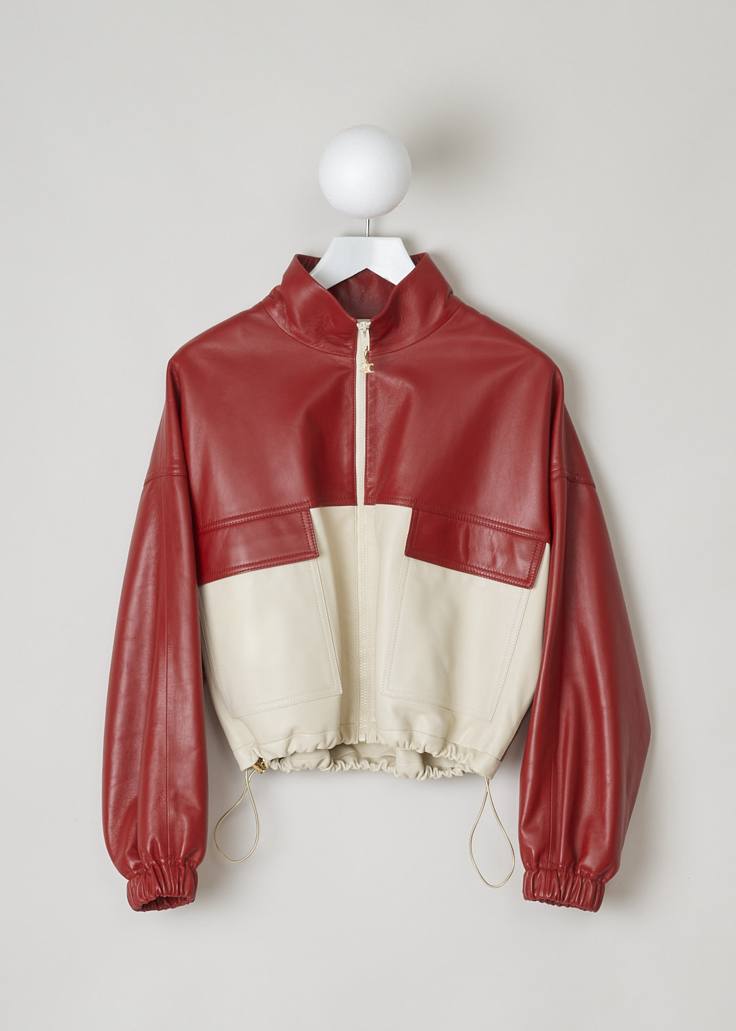 CELINE, TWO-TONE CROPPED LEATHER JACKET, 150T_2EE13_27LV, Red, Beige, Front, This cropped leather jacket is  two-toned, with the top half in lipstick red and the bottom half and the back in off-white. The jacket has a stand-up collar, two patch pockets with flap and a zipper in a matching off-white color. The gold-tone pull-tab is shaped in the brand's logo. The long sleeves have elasticated cuffs. The elasticated hemline has gold-tone cord locks on the inside. The jackets has a single inner pocket


