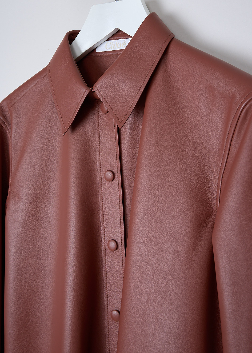 CHLOÉ, LEATHER BLOUSE IN INTENSE BROWN, CHC22SCH1620826J_INTENSE_BROWN, Brown, Detail, The long sleeve leather blouse in Intense Brown has a pointed collar and a front button placket with press studs. The long sleeves have cuffs with a press stud closure. The blouse has a rounded hemline. In the back, a seam runs along the back yoke with a centre box pleat.
