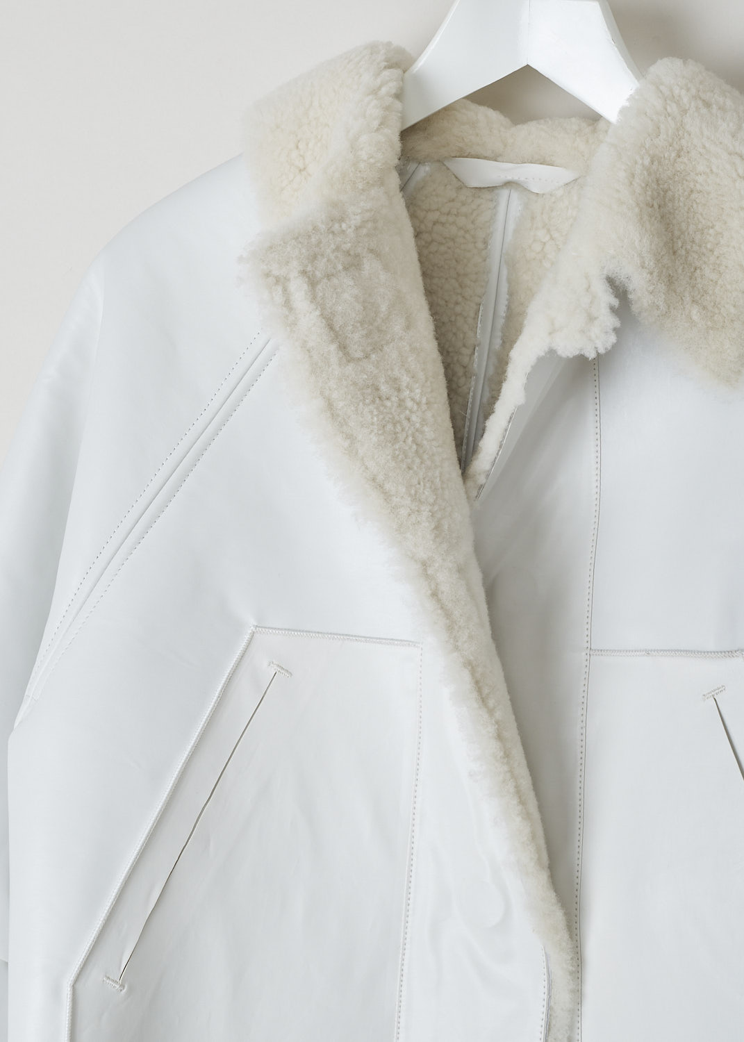 KASSL, CROPPED SHEARLING OIL WHITE COAT, C11310000W_COAT_ORIGINAL_CROPPED_SHEARLING_OIL_WHITE, White, Detail, This cropped coat is made with the brand's signature oil coated cotton-blend in white and is fully lined with shearling. The coat has a shearling spread collar, magnetic front button closure and slanted pockets. The coat is constructed with different seams, giving it a paneled look. 
