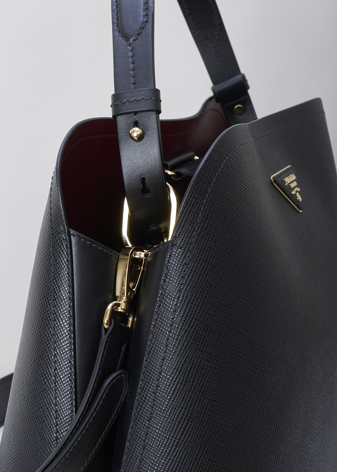 PRADA, MEDIUM MATINÃ‰E SHOULDER BAG IN BLACK, SAFFIANO_CUIR_C_1BA249_NERO_CERISE, Black, Detail, This black MatinÃ©e shoulder bag is made with Saffiano leather. Both the leather handle and shoulder strap are adjustable and detachable. The bag has gold-tone metal hardware with the brand's triangle logo plaque on the front. The open top has a magnetic snap closure in the middle. The cherry red interior has a centre zip pocket that divides the main compartment into two spacious sides. The bag has are movable leather keychain.  

