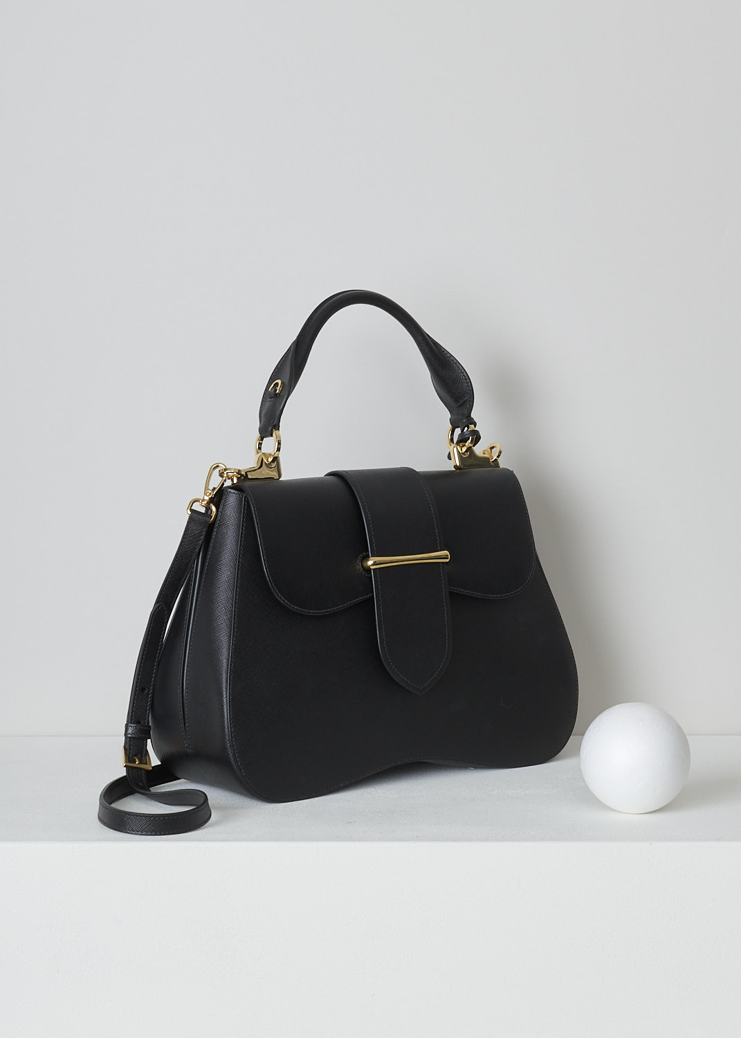 PRADA, LARGE SIDONIE TOP HANDLE BAG IN BLACK, CARTELLA_1BN002_F0002_NERO, Black, Side, This large black Sidonie Top Handle Bag is made with Saffiano leather. The bag comes with a leather handle and an adjustable and detachable shoulder strap. The bag has gold-tone metal hardware with the brand's logo on the back. The removable leather keychain has that same gold-tone logo on it. The slip-through closure opens up to reveal its red interior. The bag has a single, spacious compartment with a zipped inner pocket to one side and a patch pocket on the other side.  

