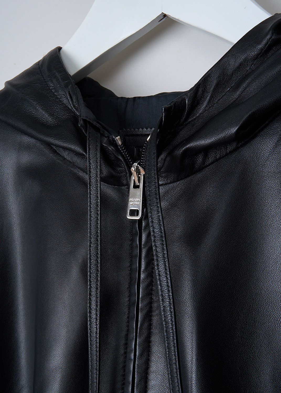 PRADA, BLACK HOODED LEATHER JACKET, 58853_JHI_F0002_NAPPA_NERO, Black, Detail, This black leather jacket has a hood with drawstrings. The jacket has a silver-tone two-way zipper in the front. Slanted welt pockets can be found in the front. The jacket has a stormflap in the front and back. The straight hemline has drawstring. The jacket has a wider silhouette. 
