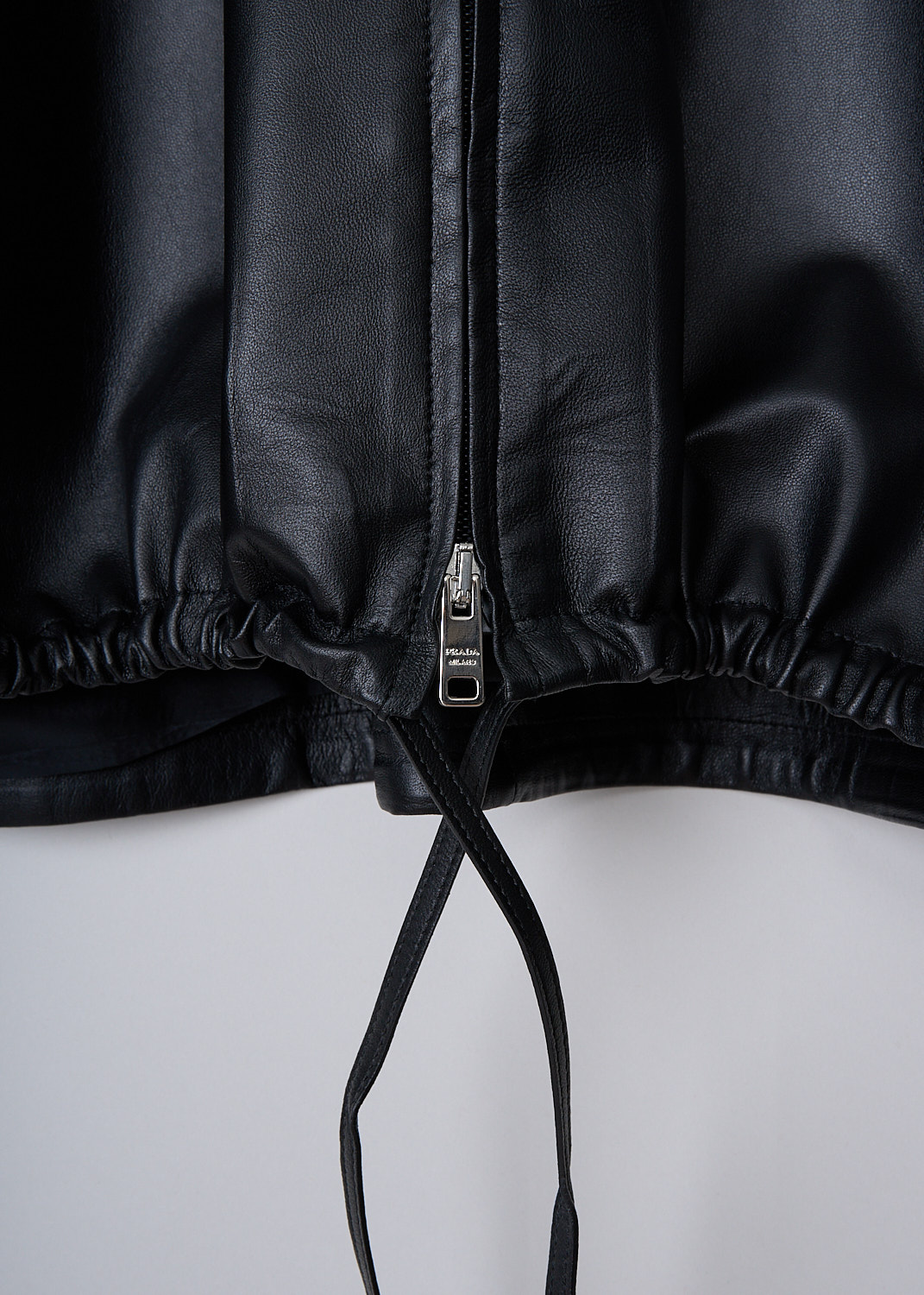 PRADA, BLACK HOODED LEATHER JACKET, 58853_JHI_F0002_NAPPA_NERO, Black, Detail 1, This black leather jacket has a hood with drawstrings. The jacket has a silver-tone two-way zipper in the front. Slanted welt pockets can be found in the front. The jacket has a stormflap in the front and back. The straight hemline has drawstring. The jacket has a wider silhouette. 
