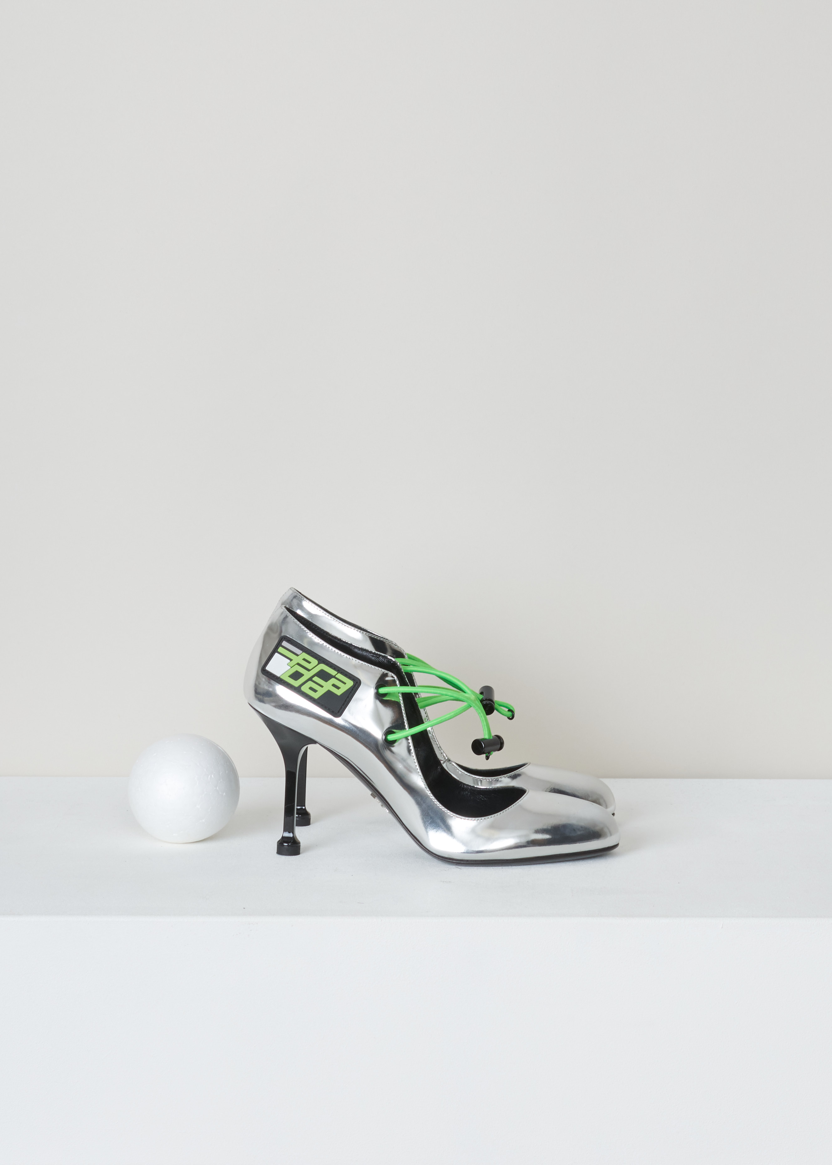 Prada Silver elastic strap mary jane Vit_Metal_1I127L_FOXNO argento verde side. Silver coated Mary Jane pumps with green elastic straps and a Prada logo patch on the side.