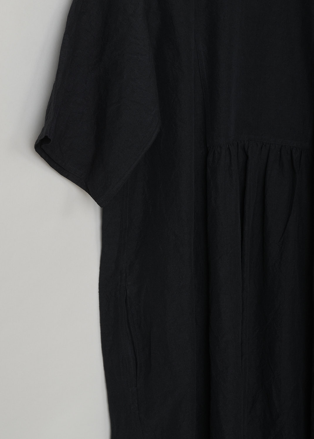 SOFIE Dâ€™HOORE, BLACK LINEN DARNELLE DRESS, DARNELLE_LIFE_BLACK, Black, Detail, This oversized black midi dress features a round neckline, dropped shoulders and short sleeves. The A-line dress has a square bib-like front with pleated details below. Concealed in the side seams, slanted pockets can be found. The dress has a straight hemline with slits on either side. 

