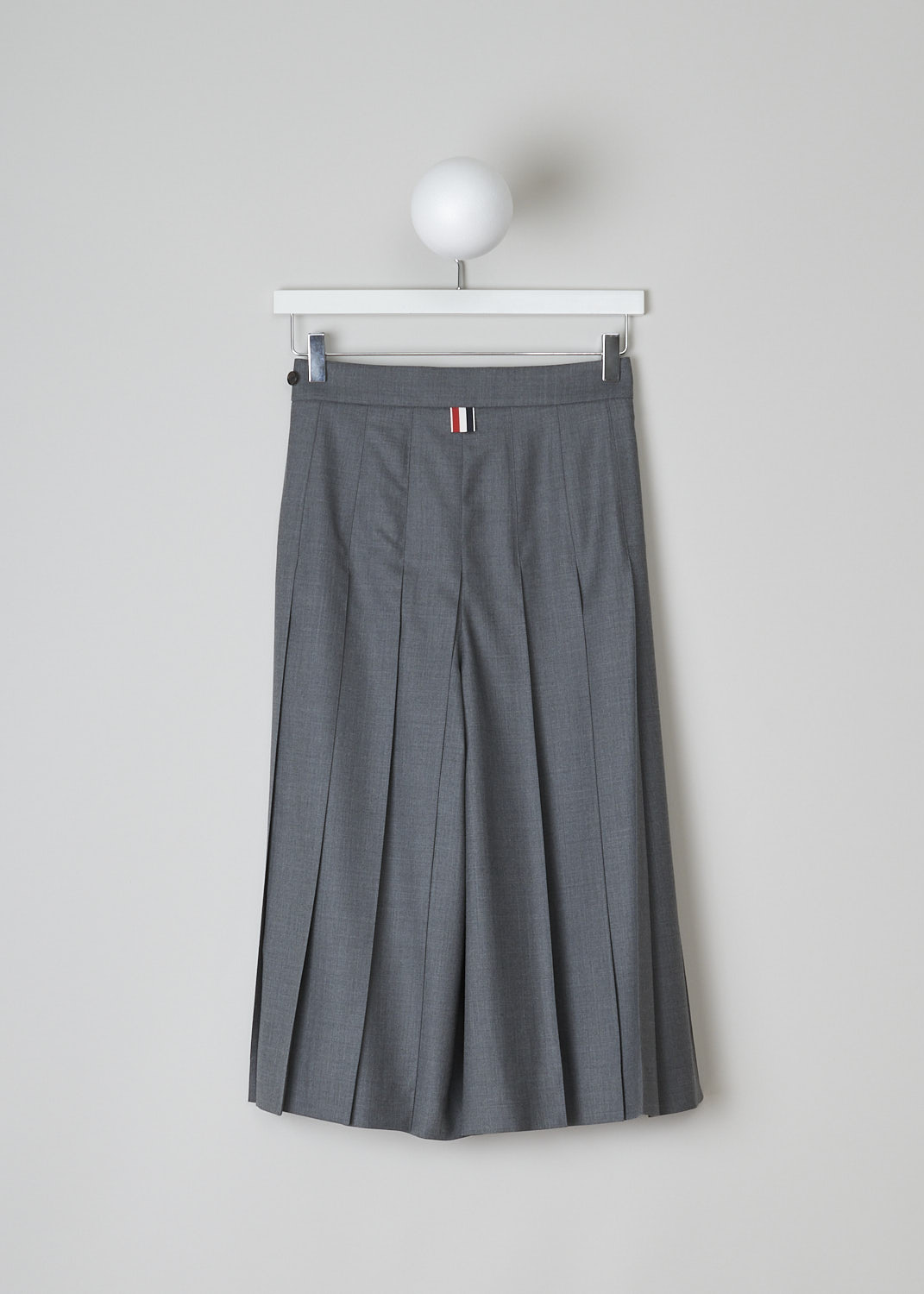 THOM BROWNE, PLEATED CULOTTES IN MID GREY, FTC379A_00626_035, Grey, Back, These mid grey pleated culottes have a concealed zip closure to one side with a button tab on the waistband. These culottes hit below the knee. In the back, the brand's signature tricolored pull-tab can be found.
