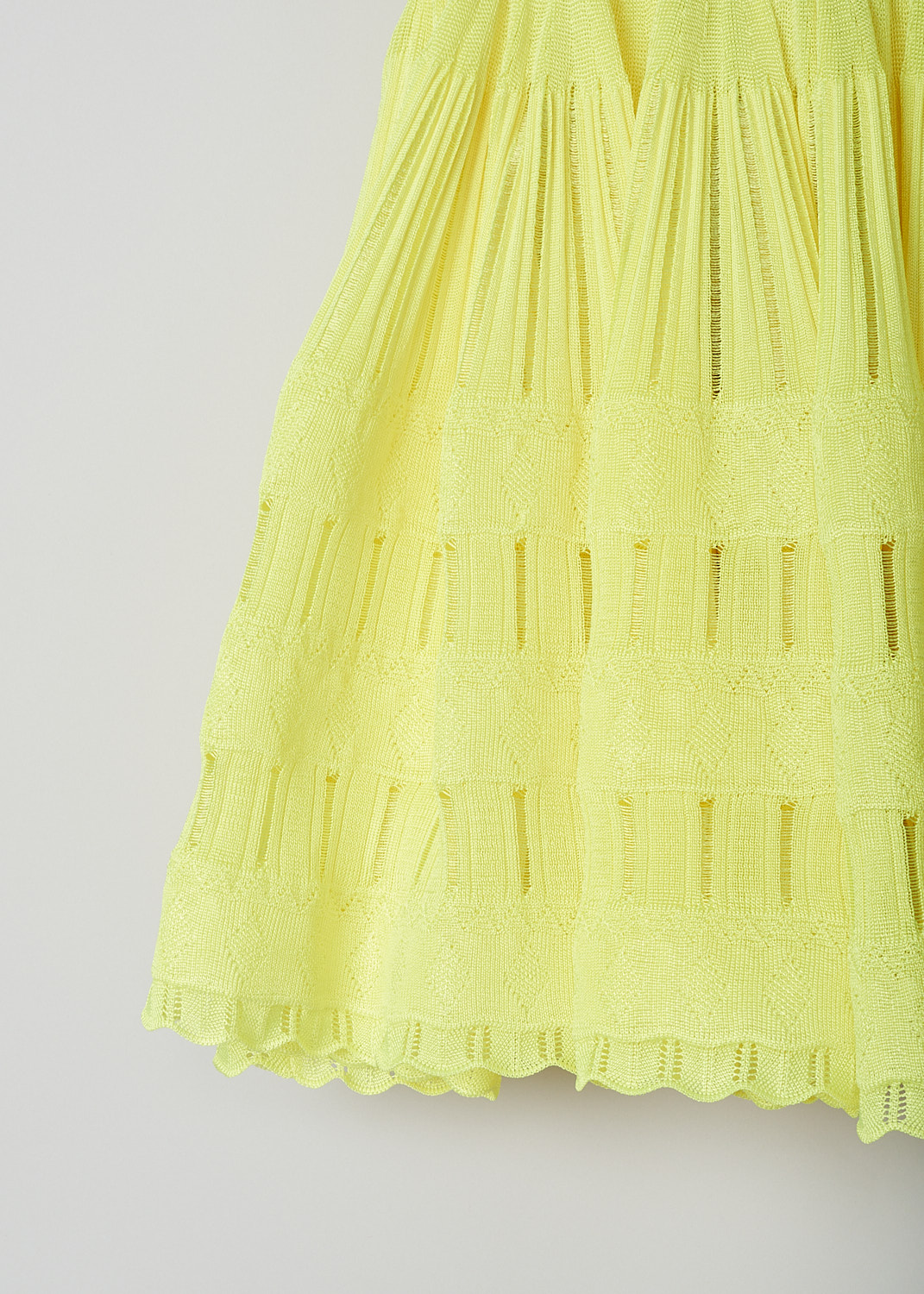 ALAÏA, FLUID SKATER DRESS IN FLUORESCENT YELLOW, AA9R22462MM712_JAUNE_FLUO, Yellow, Detail, This sleeveless skater dress in fluorescent yellow has a scooped U-neckline. The slip-on dress has a fitted bodice with vertical openwork trims, giving it a ribbed look. A broad elastic waistband divides the bodice from the voluminous mini skirt. The crinoline-like skirt has intricate openwork and lace trims. The dress has a scalloped hemline. 
