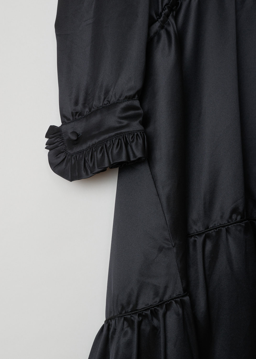 Balenciaga, Black ruffled dress, 494197_TXC02_1000, black, detail. This all black dress has a ruffled neckline and cuffs which have a single button. A cord tunnel divides the skirt from the top. The closure option on this piece is the single button on the back.
