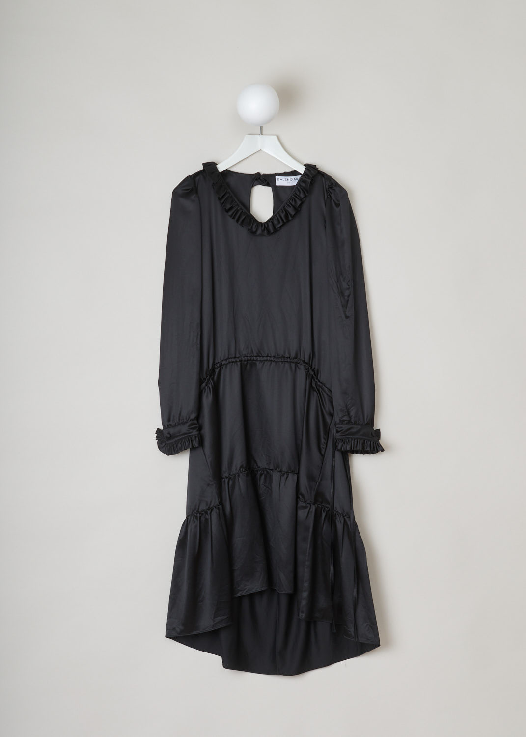 Balenciaga, Black ruffled dress, 494197_TXC02_1000, black, front. This all black dress has a ruffled neckline and cuffs which have a single button. A cord tunnel divides the skirt from the top. The closure option on this piece is the single button on the back.