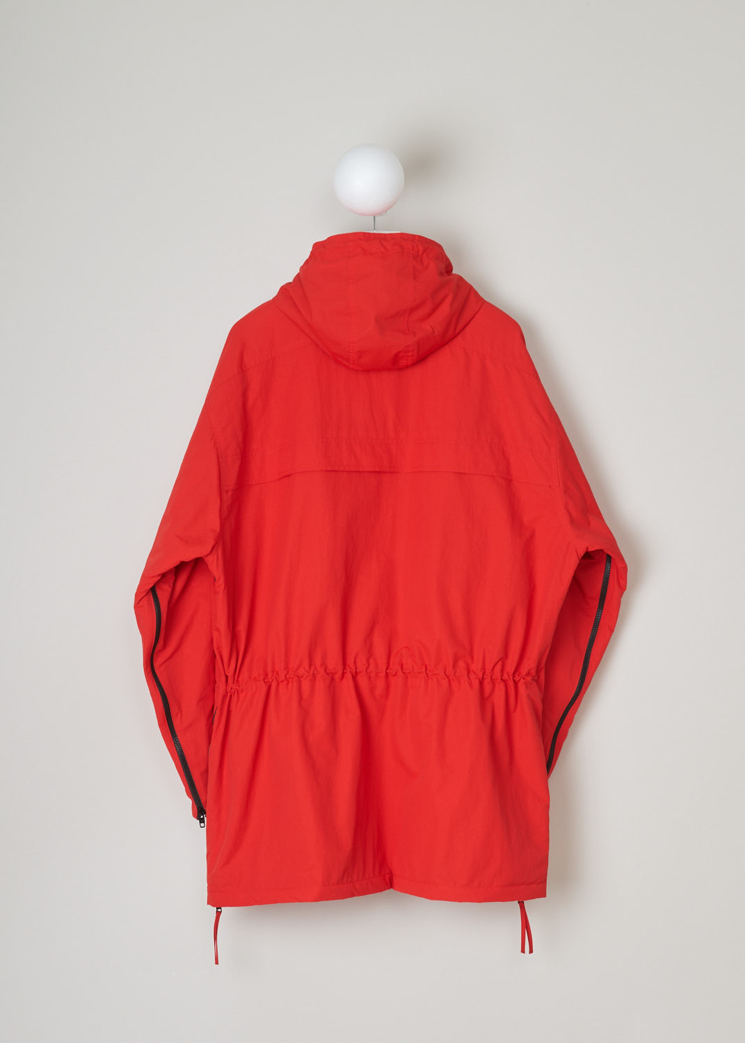 Balenciaga, Red parka model, 646774_TJ014_6400, red, back. Red oversized parka has lots of features beginning with the hood which is lined and detachable with press buttons. Going down this model has 4 pockets 2 on chest height 2 below that, with al the pockets being forward slanted. There is a cord tunnel on the inside with which the width of the waist can be adjusted. The fun part of this parka is the zipper which starts from the sides going up to the armpit and ending on the sleeves. Comes with zip fastening 