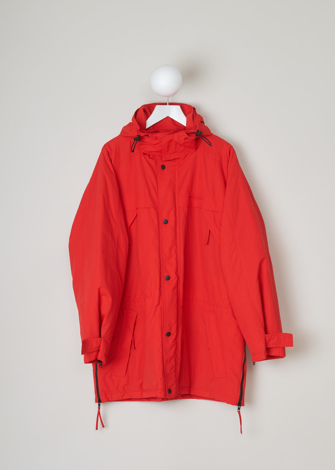 Balenciaga, Red parka model, 646774_TJ014_6400, red, front. Red oversized parka has lots of features beginning with the hood which is lined and detachable with press buttons. Going down this model has 4 pockets 2 on chest height 2 below that, with al the pockets being forward slanted. There is a cord tunnel on the inside with which the width of the waist can be adjusted. The fun part of this parka is the zipper which starts from the sides going up to the armpit and ending on the sleeves. Comes with zip fastening 