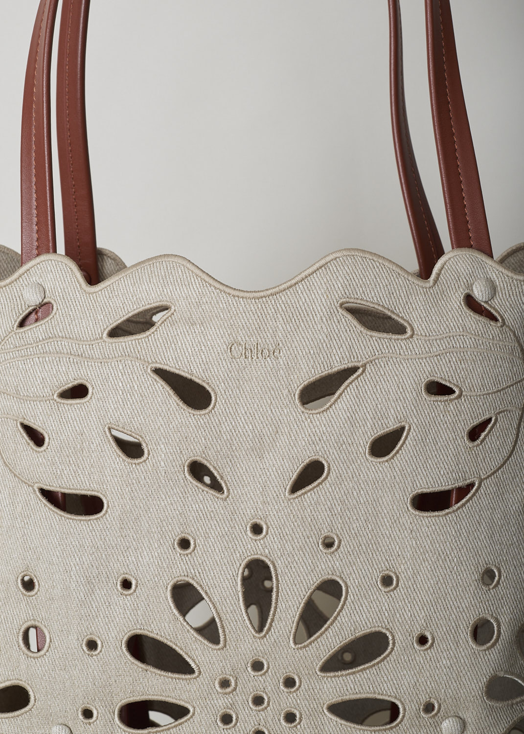 CHLOÉ LARGE KAMILLA NORTH - SOUTH TOTE BAG IN SEPIA BROWN
,CHC22SS492G2327S_KAMILLA_LARGE_NORTH_SO, Beige, Detail, This large Kamilla North - South tote bag in sepia brown has two tan leather top handles. The linen has a scalloped top edge and floral broderie anglaise detailing throughout. On the inside, the bag has a removable tan leather pouch with a zipper.  