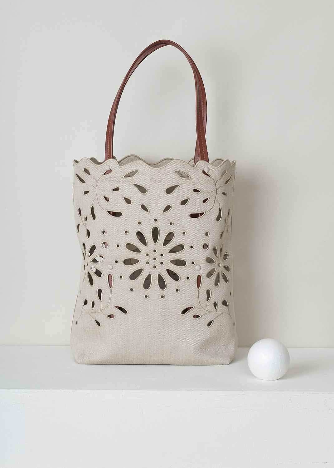 CHLOÉ LARGE KAMILLA NORTH - SOUTH TOTE BAG IN SEPIA BROWN
,CHC22SS492G2327S_KAMILLA_LARGE_NORTH_SO, Beige, Front, This large Kamilla North - South tote bag in sepia brown has two tan leather top handles. The linen has a scalloped top edge and floral broderie anglaise detailing throughout. On the inside, the bag has a removable tan leather pouch with a zipper.  