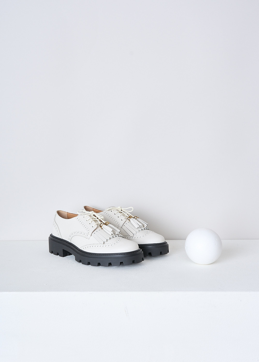 TODS, OFF-WHITE LOAFERS WITH TASSELS, XXW08J0HO10RBTB015, White, Front, These off-white leather derby shoes have a front lace-up closure. The off-white laces have tasseled tips. These shoes have a round toe with fringes across the vamp. Classic perforation detailing extends along the entire shoe. These shoes have a ridged black sole.


