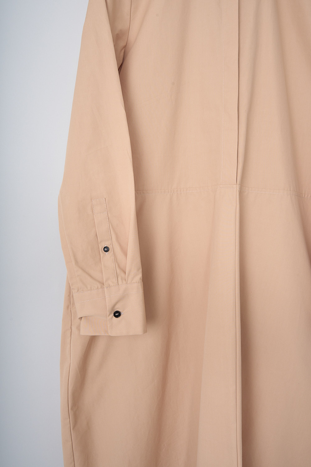 JIL SANDER, DARK BEIGE POPLIN MAXI DRESS, J04CT0007_J45002_259, Beige, Detail, This dark beige poplin maxi dress has a spread collar and a concealed partial button placket. The long sleeves have buttoned cuffs. A horizontal seam divides the top half from the maxi skirt. Slanted pockets are concealed in the side seams. In the back, a knife pleat runs vertically along the length of the dress ending in a centre slit. The hemline has an asymmetric finish. The dress has a wide silhouette.  
