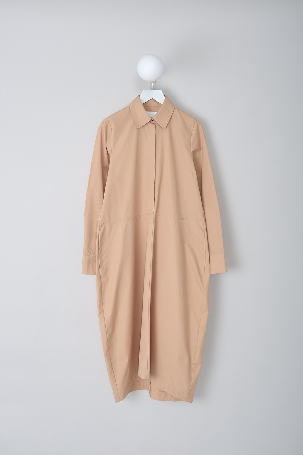 JIL SANDER, DARK BEIGE POPLIN MAXI DRESS, J04CT0007_J45002_259, Beige, Front, This dark beige poplin maxi dress has a spread collar and a concealed partial button placket. The long sleeves have buttoned cuffs. A horizontal seam divides the top half from the maxi skirt. Slanted pockets are concealed in the side seams. In the back, a knife pleat runs vertically along the length of the dress ending in a centre slit. The hemline has an asymmetric finish. The dress has a wide silhouette.  
