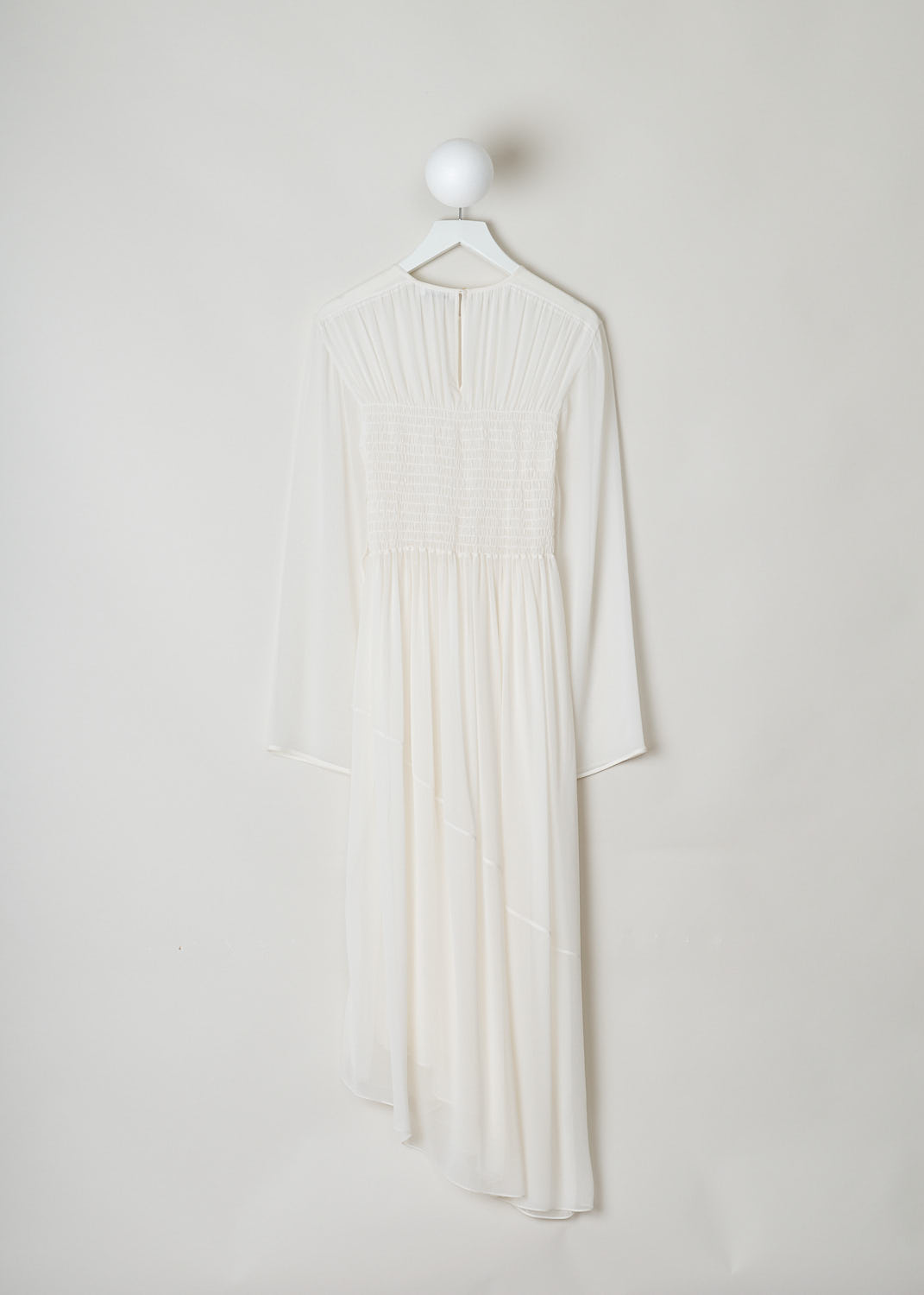 JIL SANDER, WHITE DRESS WITH SHIRRED BODICE, White, Back, This white long sleeve dress has pleats across the chest and a shirred bodice. The dress is made in a semi sheer fabric.  The skirt flows out from small crystal pleats. The hemline has an asymmetric finish, meaning that from left to right one side is longer than the other. A single button can be found in the back of the neck.
