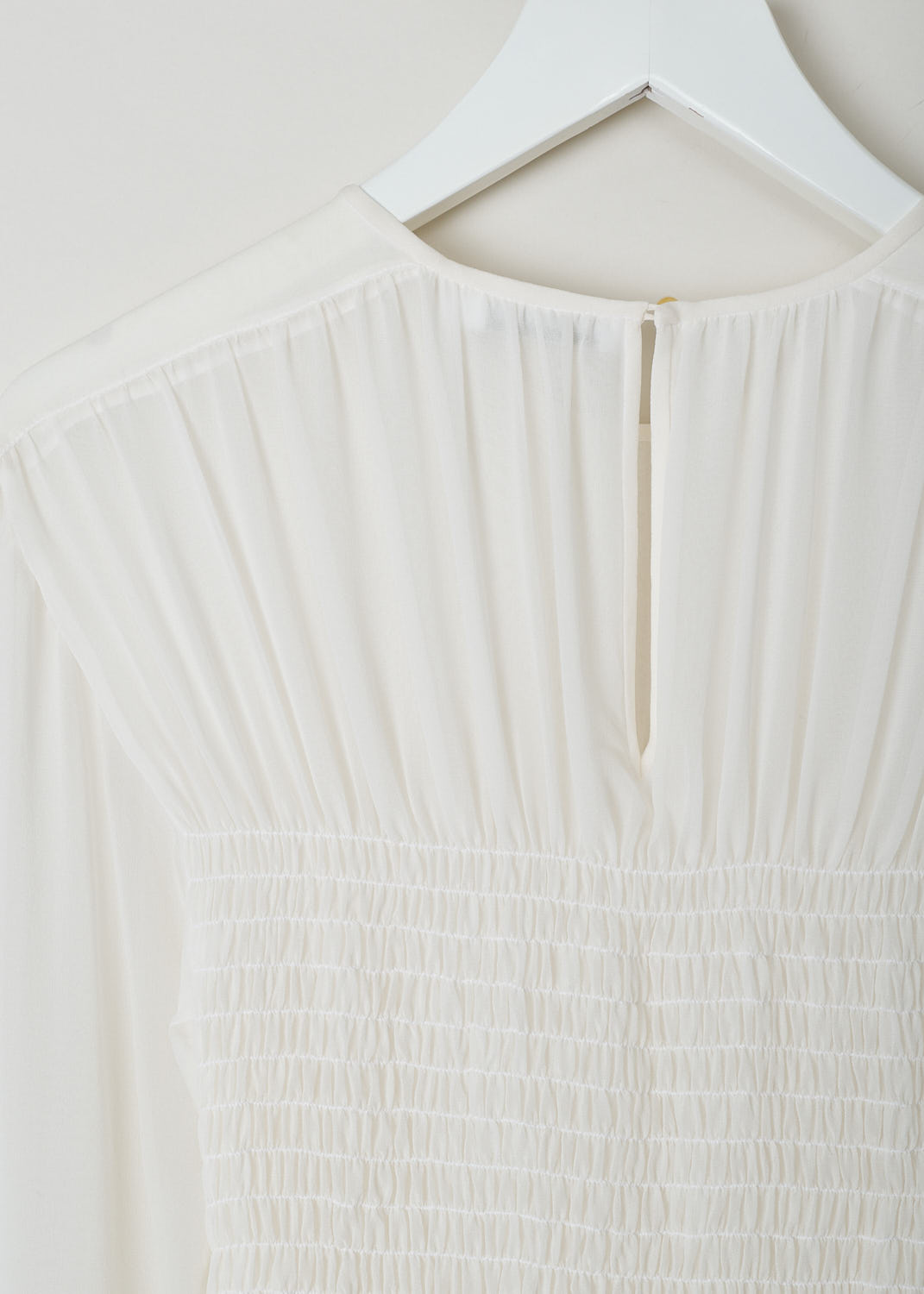 JIL SANDER, WHITE DRESS WITH SHIRRED BODICE, White, Detail 1, This white long sleeve dress has pleats across the chest and a shirred bodice. The dress is made in a semi sheer fabric.  The skirt flows out from small crystal pleats. The hemline has an asymmetric finish, meaning that from left to right one side is longer than the other. A single button can be found in the back of the neck.
