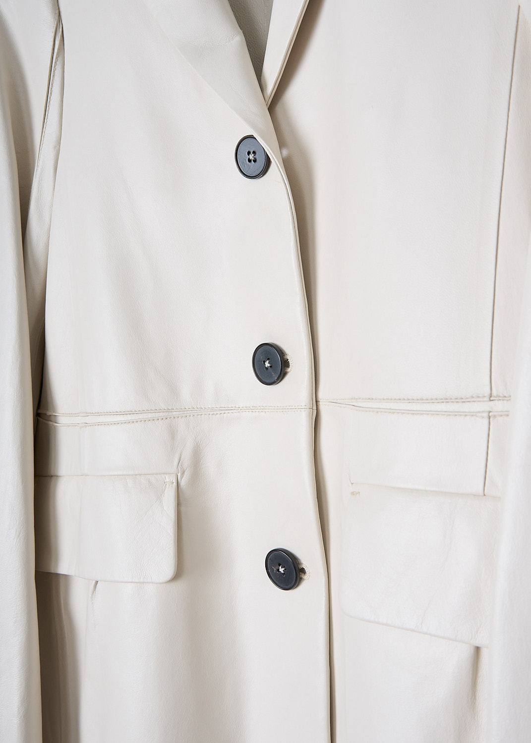 JIL SANDER, SINGLE-BREASTED WHITE LEATHER JACKET, JSWM651575_WML01071_104, White, Detail, This off-white leather jacket has a notched lapel and a front button closure with dark colored buttons. On the front, the jacket has two flap welt pockets. The long sleeves has straight ends. A decorative seam runs horizontally across the front and back. The jacket has a straight hemline. 

