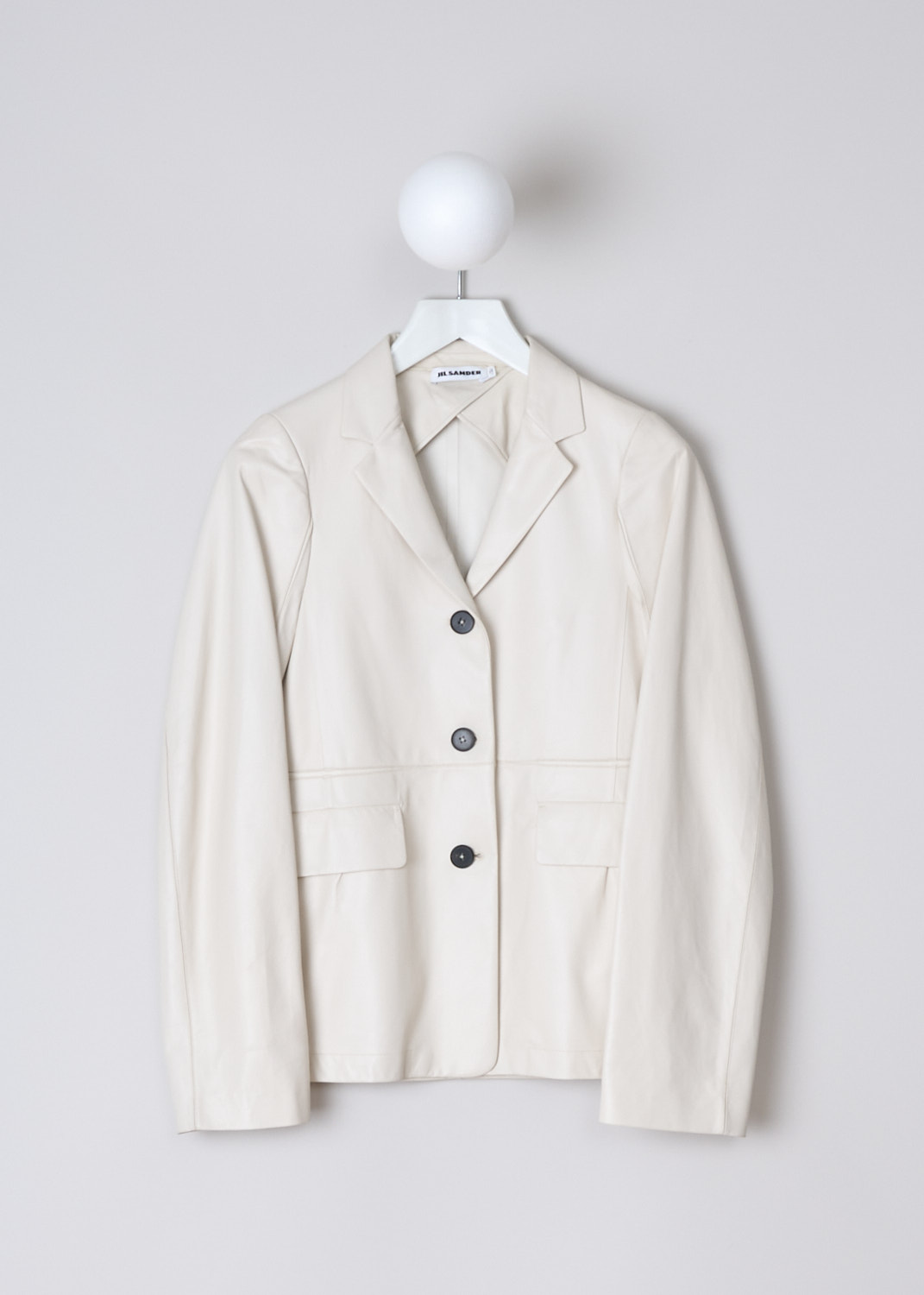 JIL SANDER, SINGLE-BREASTED WHITE LEATHER JACKET, JSWM651575_WML01071_104, White, Front, This off-white leather jacket has a notched lapel and a front button closure with dark colored buttons. On the front, the jacket has two flap welt pockets. The long sleeves has straight ends. A decorative seam runs horizontally across the front and back. The jacket has a straight hemline. 

