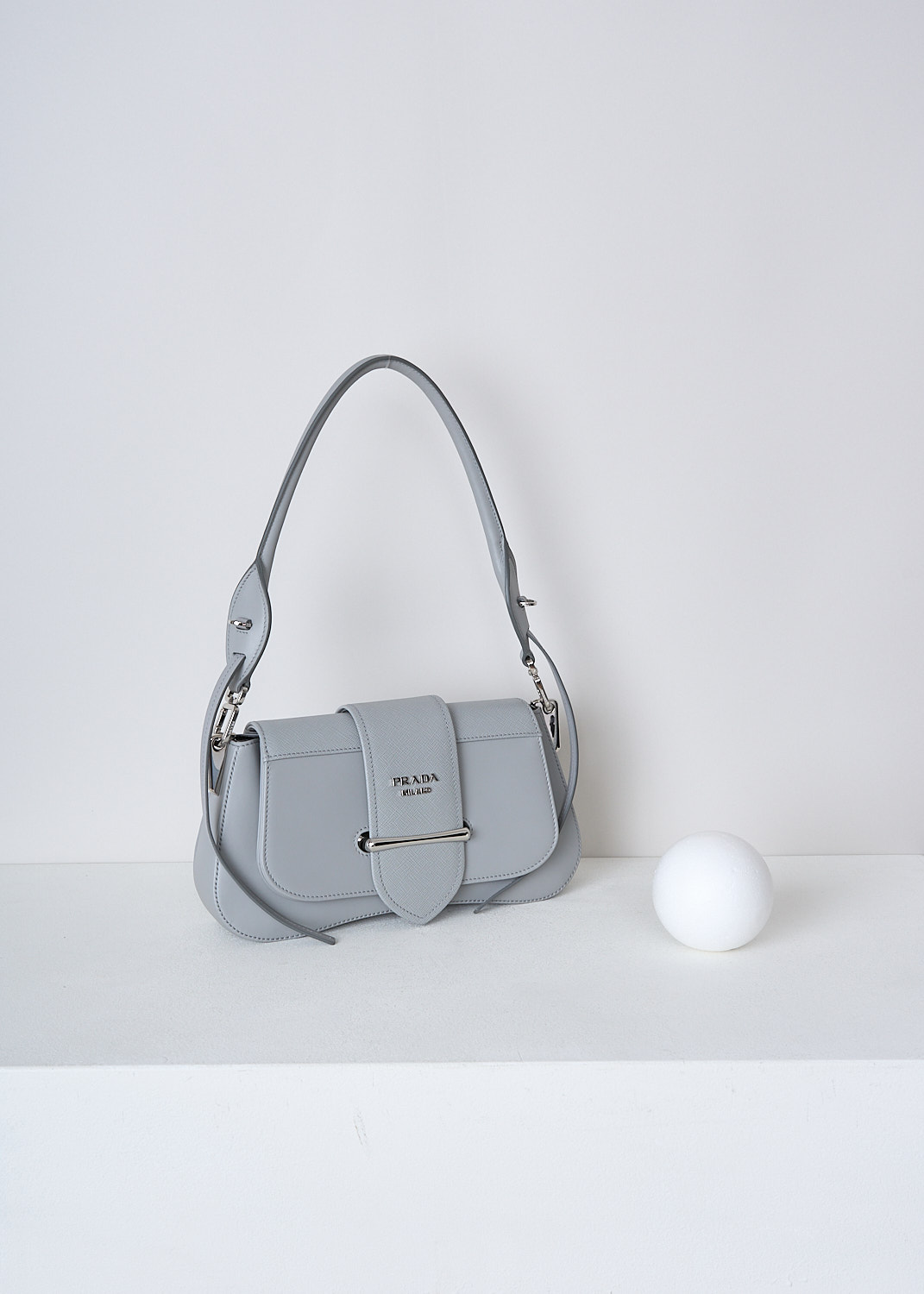 PRADA, SIDONIE SHOULDER BAG IN NUBE, 2BB0_CITY_CALF_SAFFI_1BD228_F0424_NUBE, Grey, Side, This Sidonie shoulder bag in the color Nube is made with both smooth and grained Saffiano leather. The bag comes witha detachable leather top handle with decorative leather straps and an adjustable and detachable shoulder strap. The bag has silver-tone metal hardware with the brand's logo on the front. The slip-through closure opens up to reveal the spacious compartment with a single patch pocket.  

