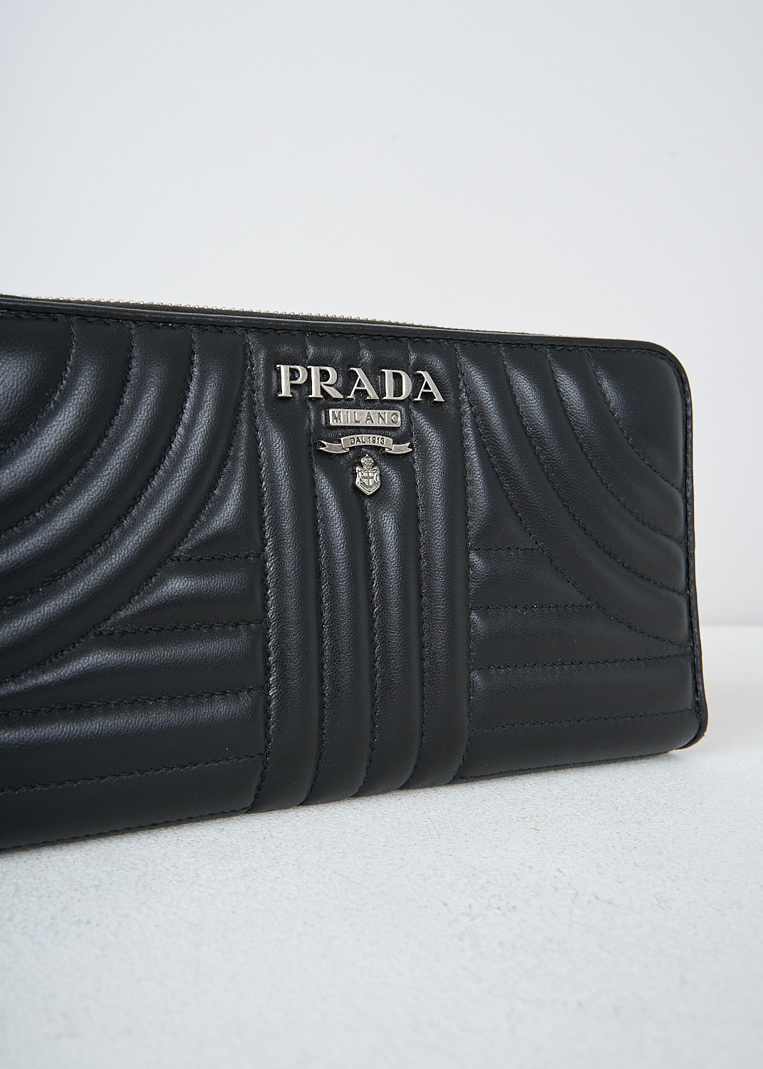 Prada, Black wallet with quilted pattern, 2B0X_NAPPA_IMPUNTURE_1ML506_F0002, Black, Detail, This black quilted wallet has a metal logo on the front. The silver-tone zipper opens up to the three bill compartments and a  zipper coin pocket. The wallet has multiple card-slots.
