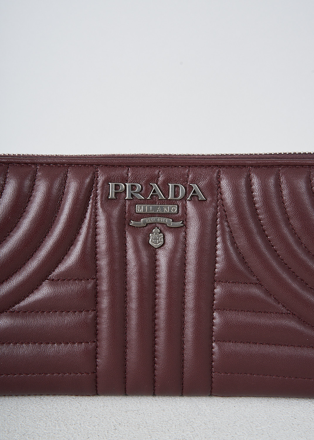 Prada, Bordeaux red wallet with quilted pattern, 2B0X_NAPPA_IMPUNTURE_1ML506_F0XJE, Red, Detail, This bordeaux red quilted wallet has the brand's metal logo on the front. The silver-tone zipper opens up to three bill compartments and a zipped coin pocket. The wallet has multiple card-slots.