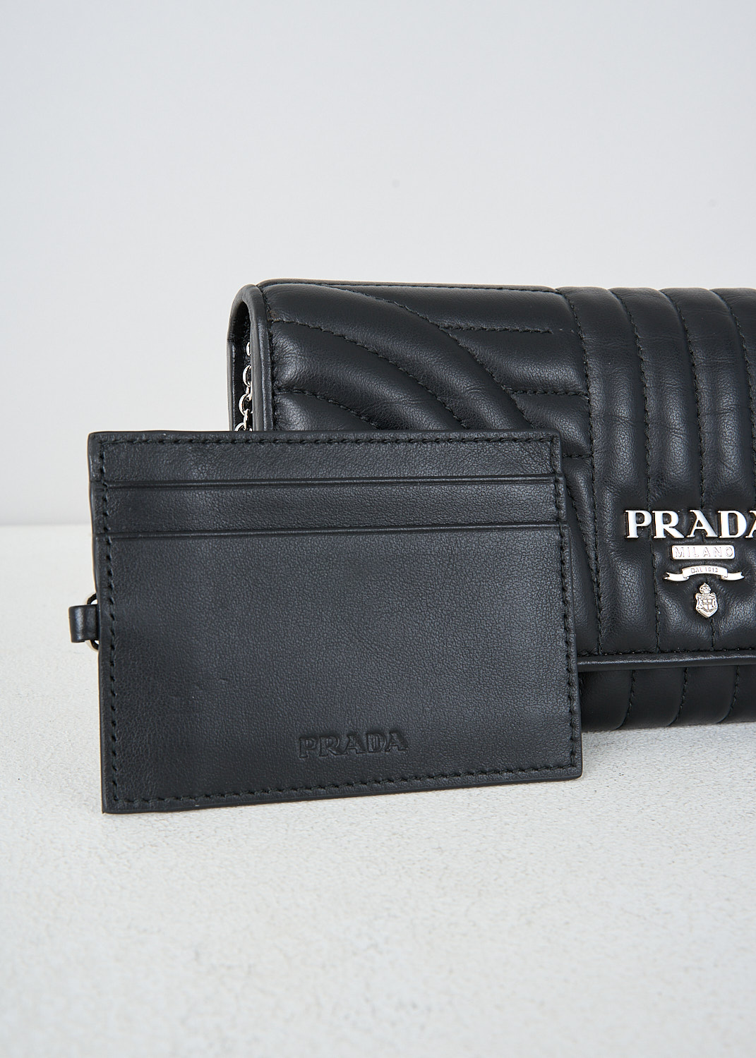 Prada, Black wallet with quilted pattern, 2D91_SOFT_CALF_IMPUN_1MH132_F0002, Black, Detail, This black quilted wallet has that brand's metal logo on the front. The wallet has a fold-over flap with press studs closure that opens up to two bill compartments and a zipper coin pocket. The wallet has multiple card-slots and a detachable card slot on a chain.