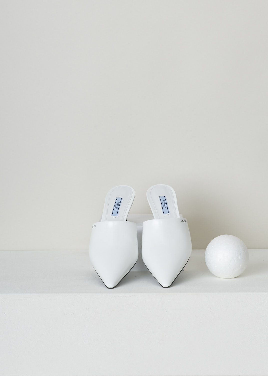 PRADA, WHITE POINTED MULES WITH HEEL, SPAZZOLATO_1S520M_F0009_BIANCO,  White, Top, These white leather mules have a pointed toe and mid-high stiletto heel. These slip-on mules have a contrasting black sole and heel tip. Along the topline, the brand name can be found in black.
