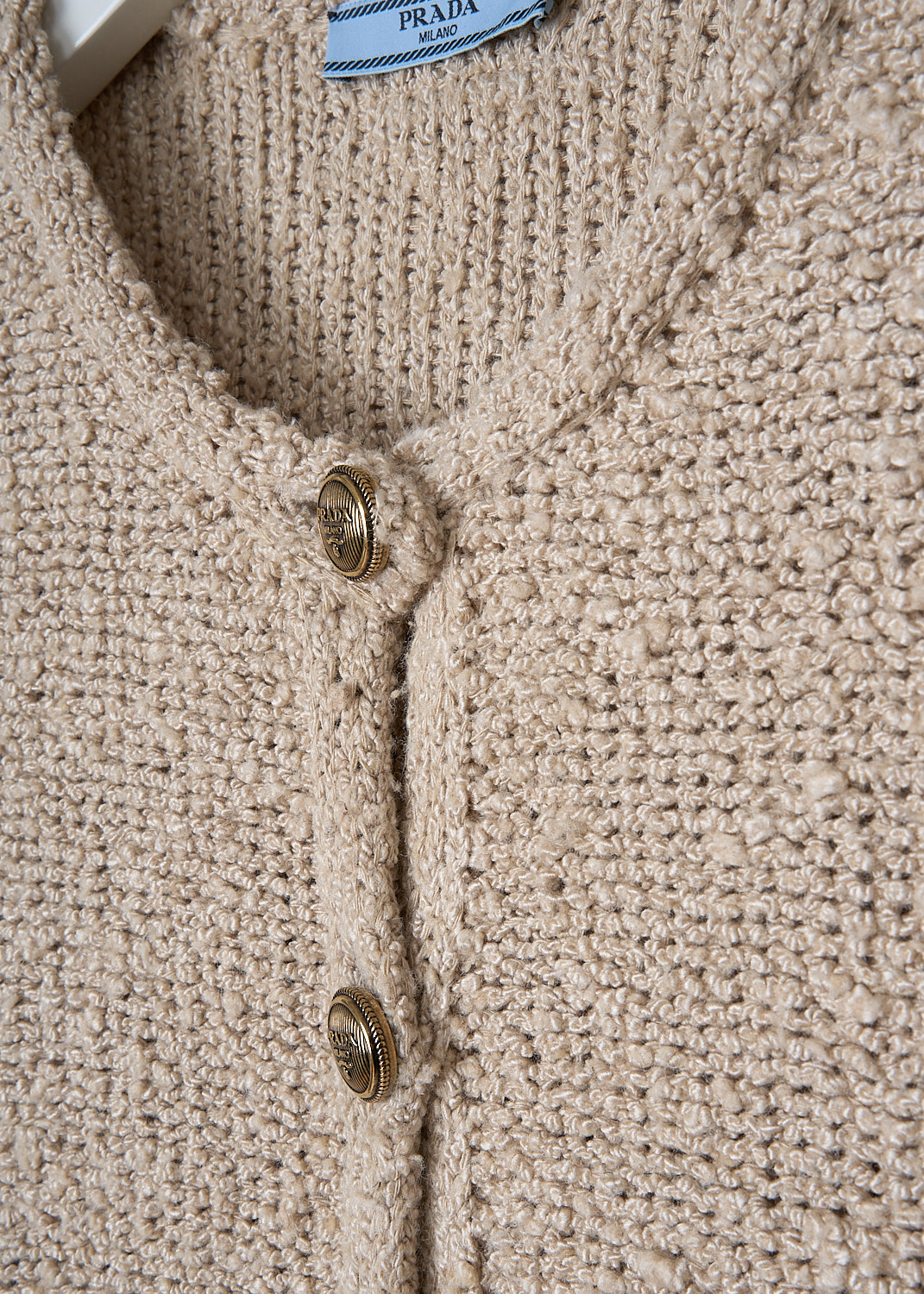 PRADA, SILK BOUCLÉ CARDIGAN IN NATURAL, P25L72_12ZD_F0018_NATURALE_, Beige, Detail, This beige silk bouclé cardigan has a round neckline and a front button closure with embossed gold-tone buttons. The cardigan has three-quarter sleeves. On the front, the cardigan has two patch pockets with those same embossed buttons. The cardigan has a cropped length. In the back, a logo patch can be found. 
