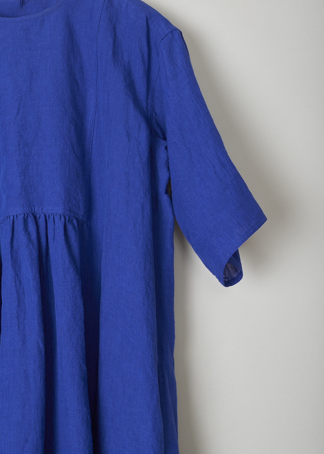 SOFIE D’HOORE, ROYAL BLUE LINEN DARNELLE DRESS, DARNELLE_LIFE_TOUAREG, Blue, Detail, This oversized royal blue midi dress features a round neckline, dropped shoulders and short sleeves. The A-line dress has a square bib-like front with pleated details below. Concealed in the side seams, slanted pockets can be found. The dress has a straight hemline with slits on either side. 

