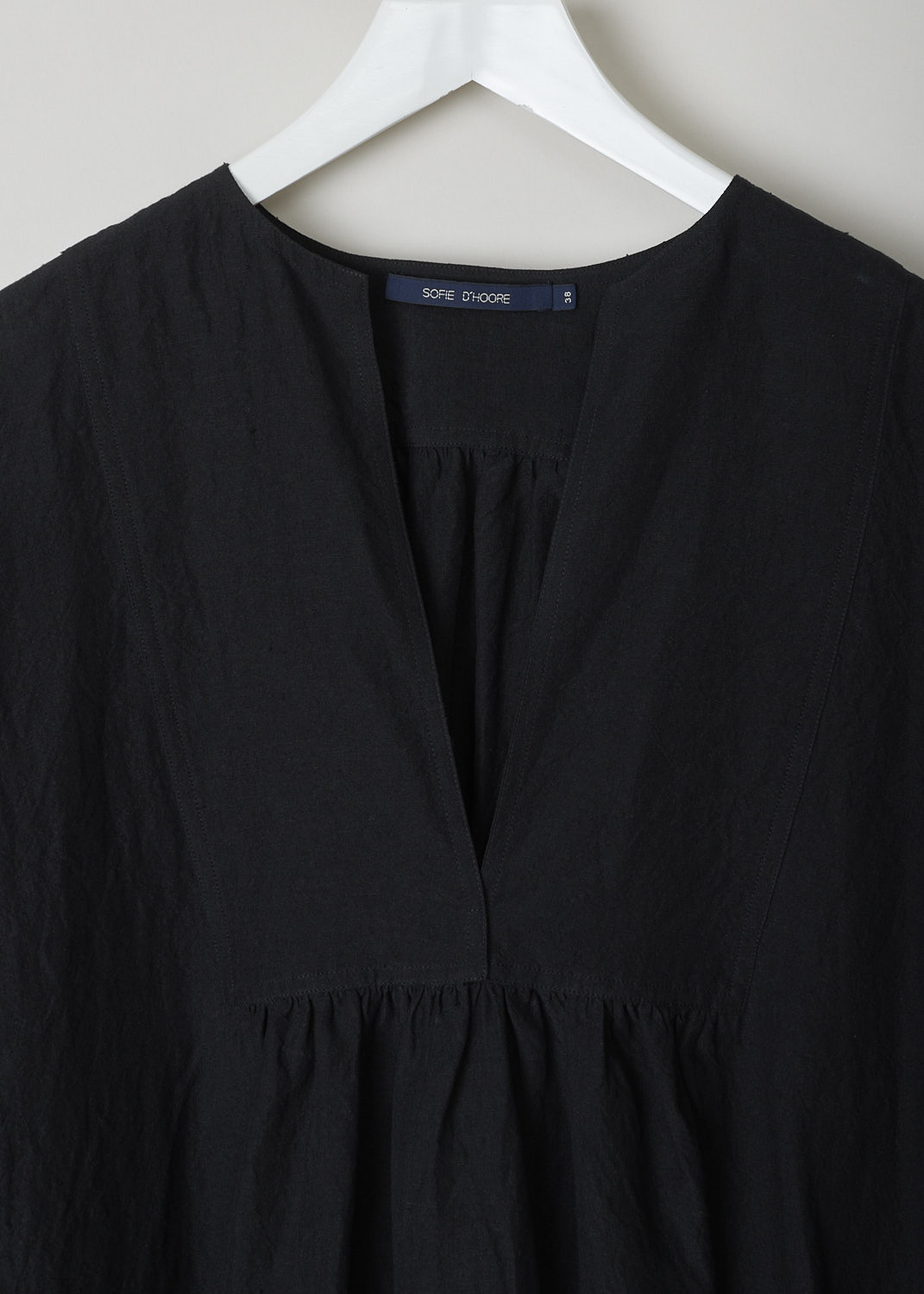 SOFIE D’HOORE, BLACK LINEN DELIZA DRESS, DELIZA_LIFE_BLACK, Black, Detail,This black linen dress has a round neckline that goes into a deep V cutout. Subtle ruching can be found beneath the V. This long sleeve midi dress has a straight hemline with an asymmetrical finish, meaning the back is a little longer than the front. The dress has concealed slanted pockets and slits can be found on either side. The dress has a wide silhouette. 
