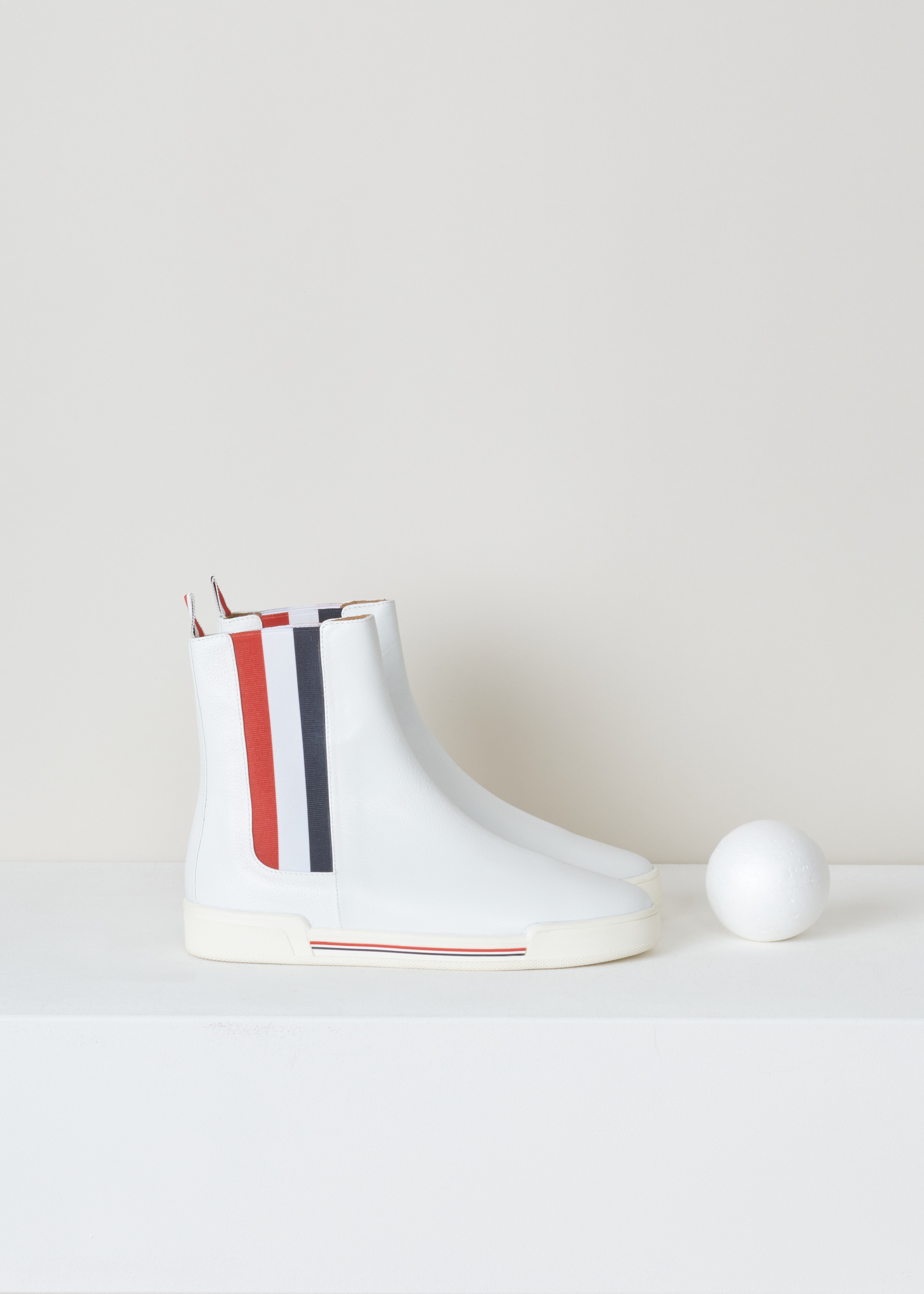 Thom Browne Chelsea boot sneaker white FFB056B_03542_100 white side. White leather chelsea boot with red and blue striped elastic side panels, a rounded toe, a pull tab at the back and a white rubber sole with red and blue detailing. 