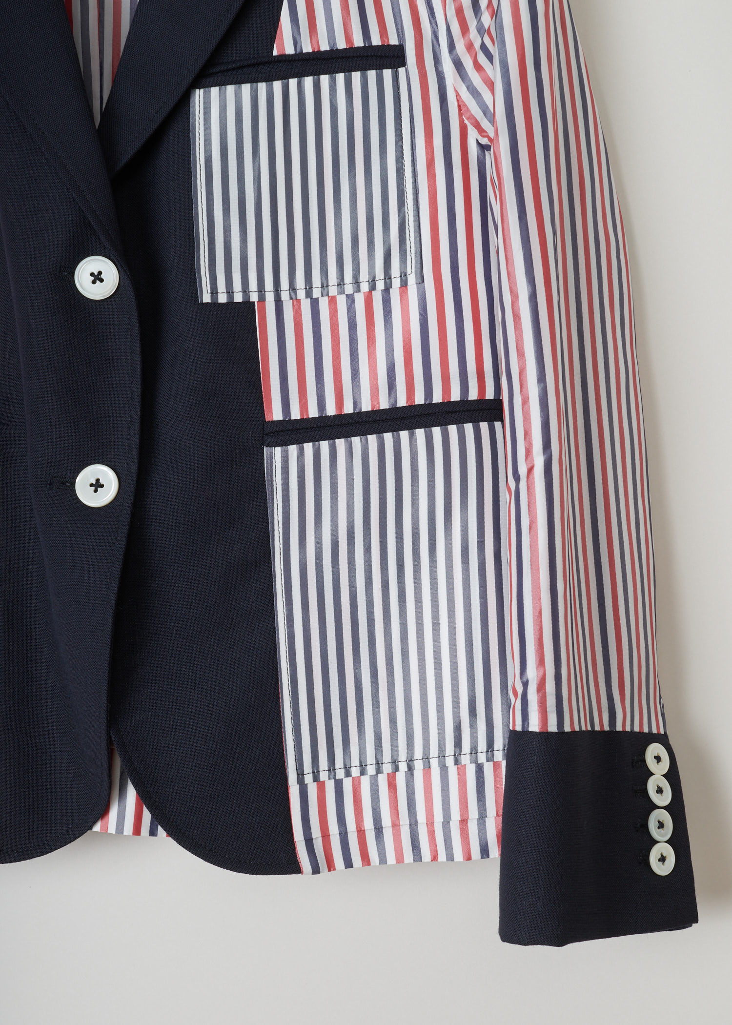 Thom Browne, Red and blue striped jacket, FBC510A_00473_415_navy, red white blue, detail1. This inside out jacket features a regular collar and a notched lapel. Going further down the long sleeves, you will find four buttoned cuffs. It has a single chest pocket and below that two jetted pockets. The jacket comes with the signature grosgrain  tab on the back.