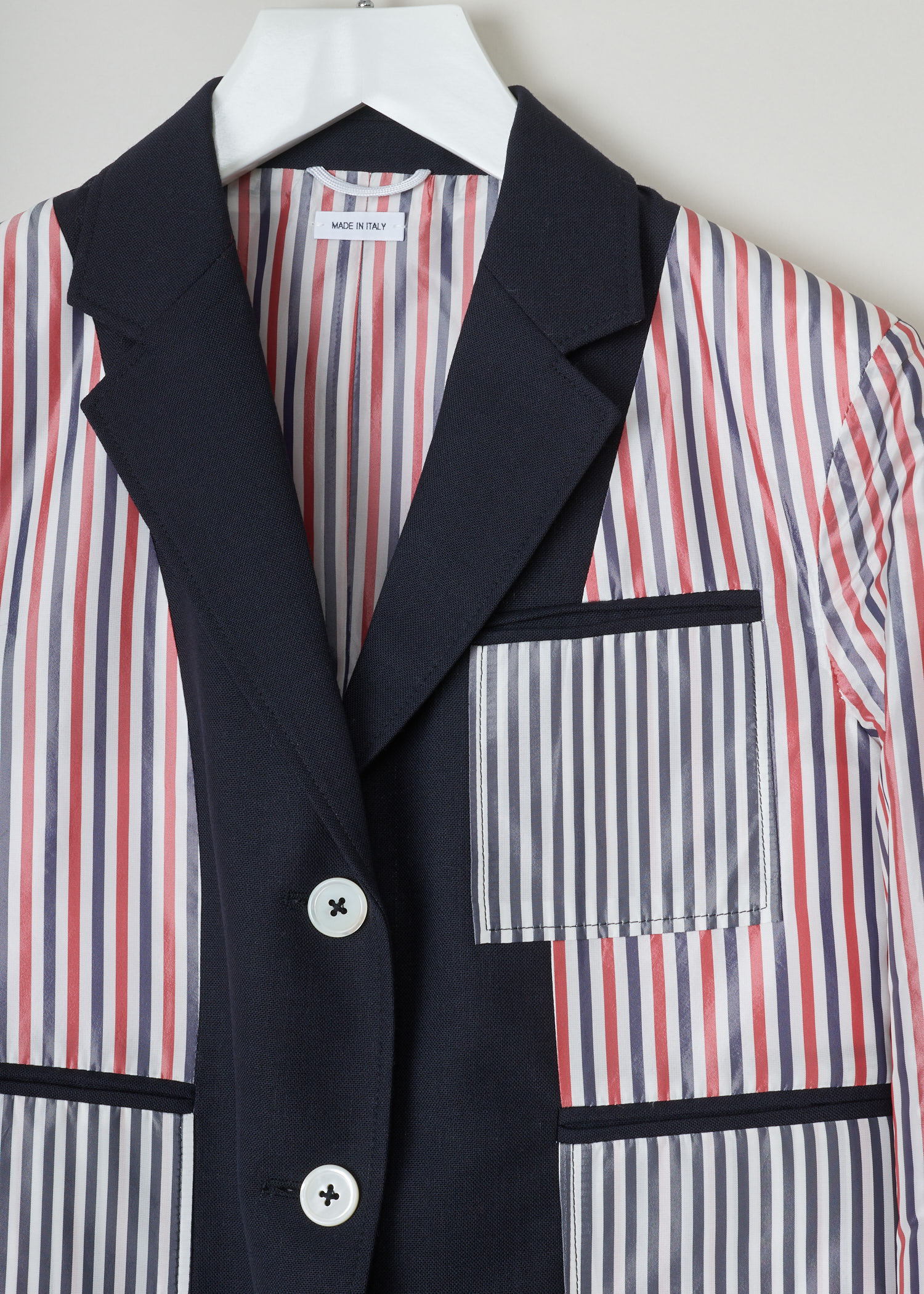 Thom Browne, Red and blue striped jacket, FBC510A_00473_415_navy, red white blue, detail2. jetted pockets. This inside out jacket features a regular collar and a notched lapel. Going further down the long sleeves, you will find four buttoned cuffs. It has a single chest pocket and below that two jetted pockets. The jacket comes with the signature grosgrain  tab on the back.