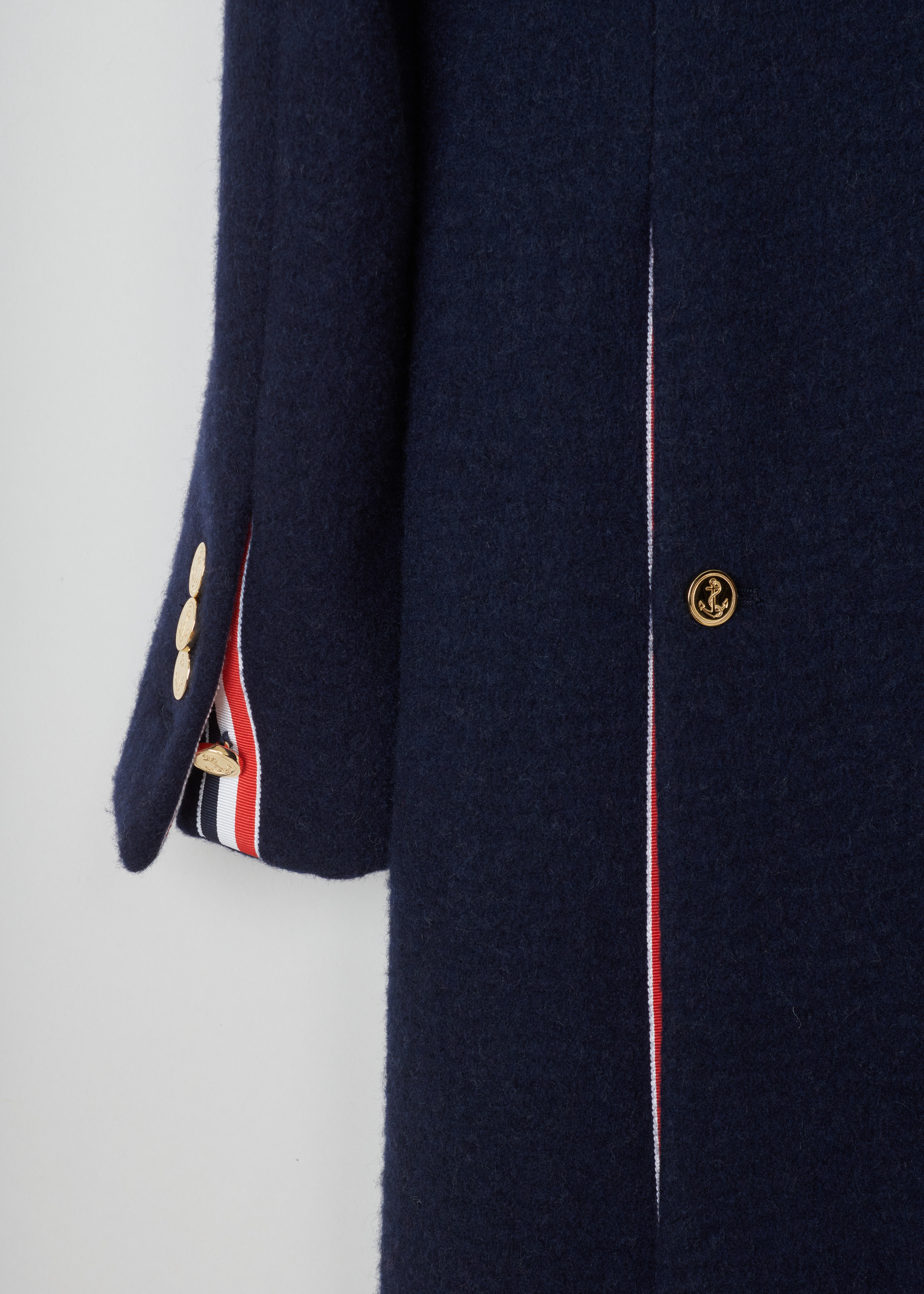 Thom Browne Navy woolen A-line coat FOC411C_03564_415_Navy detail. Wool and cashmere blend coat in a classic silhouet with the iconic Thom Browne stripes on the back, a squared collar, concealed button fastening with one visible gold button and two side pockets.