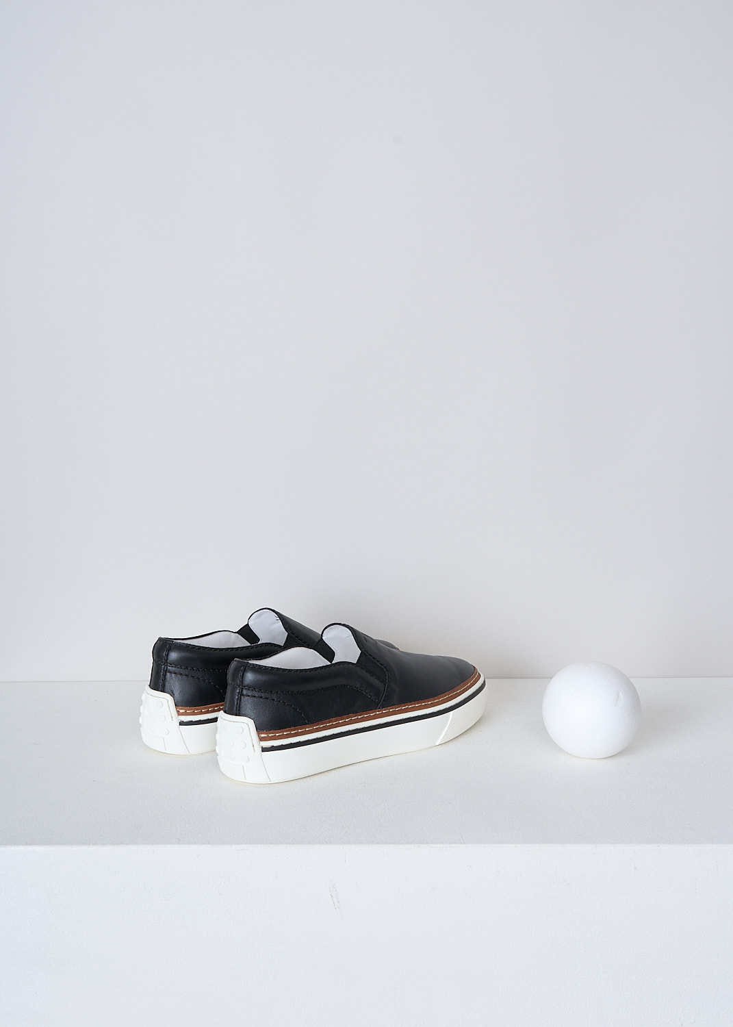 TODS, BLACK LEATHER SLIP-ON SHOES, XXW22K0FK70QPJB999_NERO, Black, Back, These slip-on shoes have a black leather top with elasticated inserts on either sides. The brand's logo can be found debossed on the front. These shoes have a broad white rubber sole with a brown, white and black trim. 
