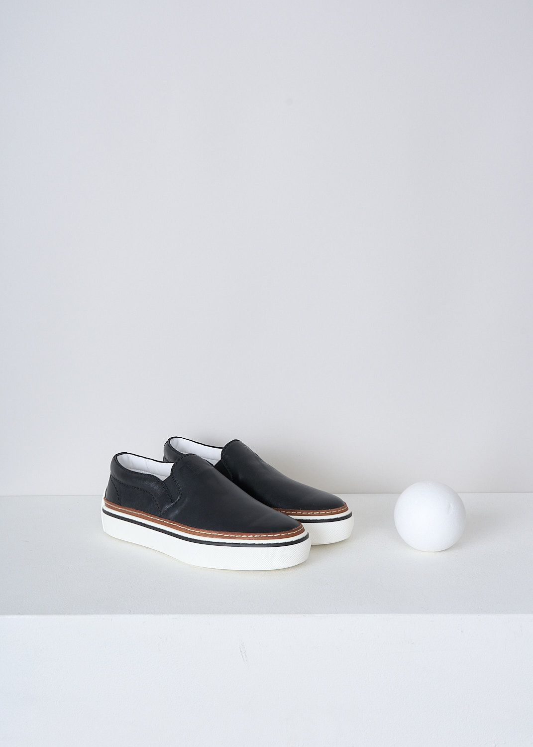 TODS, BLACK LEATHER SLIP-ON SHOES, XXW22K0FK70QPJB999_NERO, Black, Front, These slip-on shoes have a black leather top with elasticated inserts on either sides. The brand's logo can be found debossed on the front. These shoes have a broad white rubber sole with a brown, white and black trim. 
