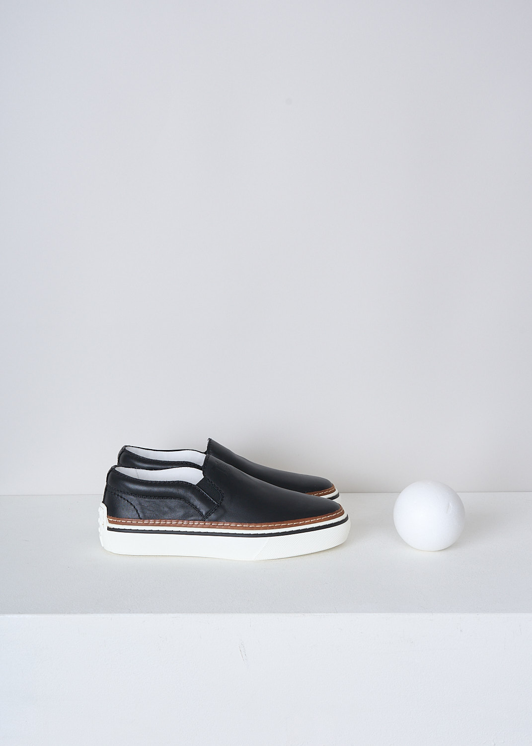 TODS, BLACK LEATHER SLIP-ON SHOES, XXW22K0FK70QPJB999_NERO, Black, Side, These slip-on shoes have a black leather top with elasticated inserts on either sides. The brand's logo can be found debossed on the front. These shoes have a broad white rubber sole with a brown, white and black trim. 
